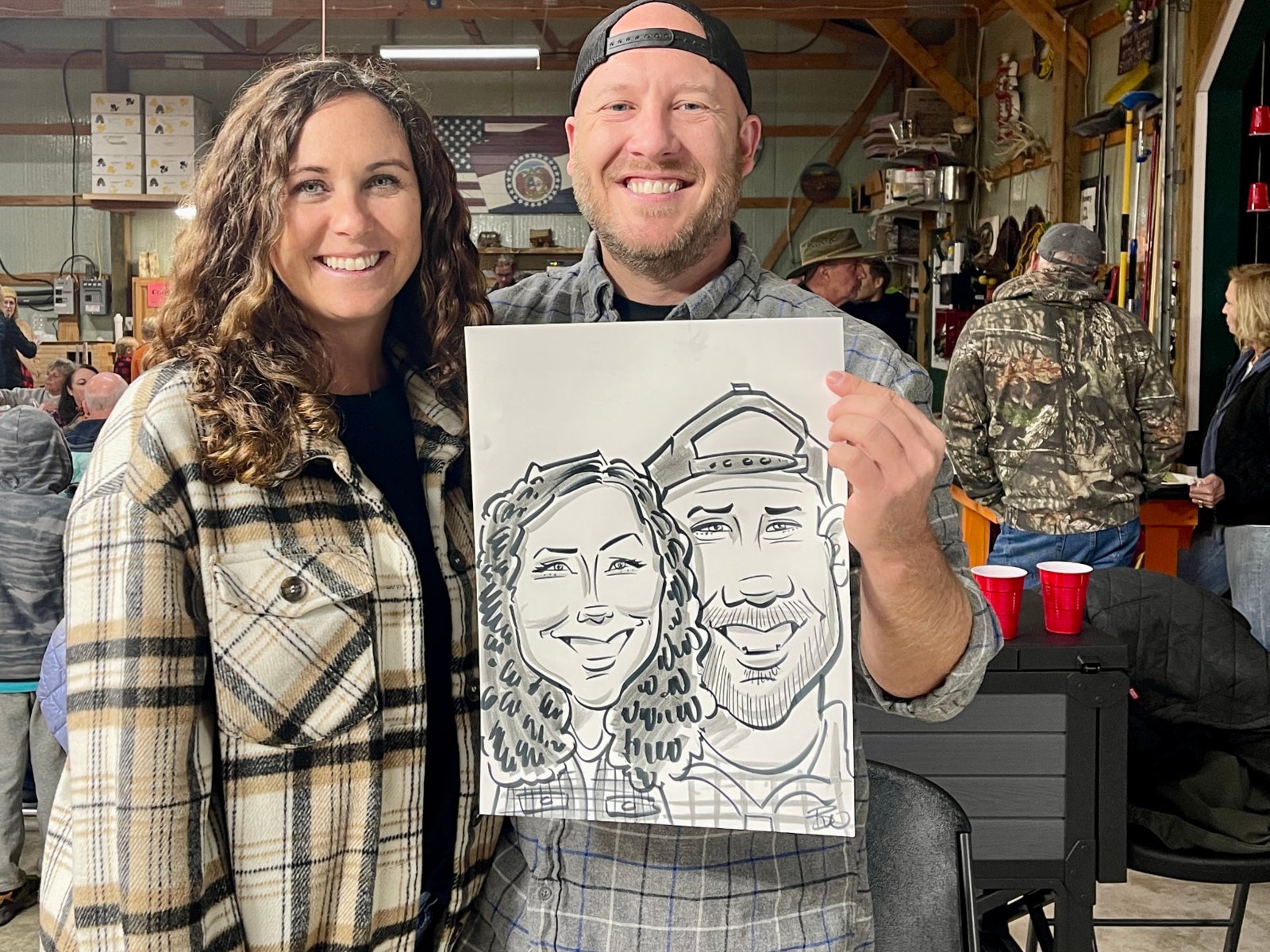 Smiling couple holding their finished black-marker caricature at a party